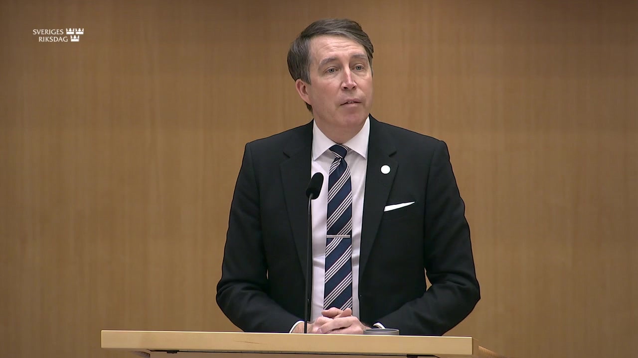 Richard Jomshof speaking at a lectern in the Riksdag.