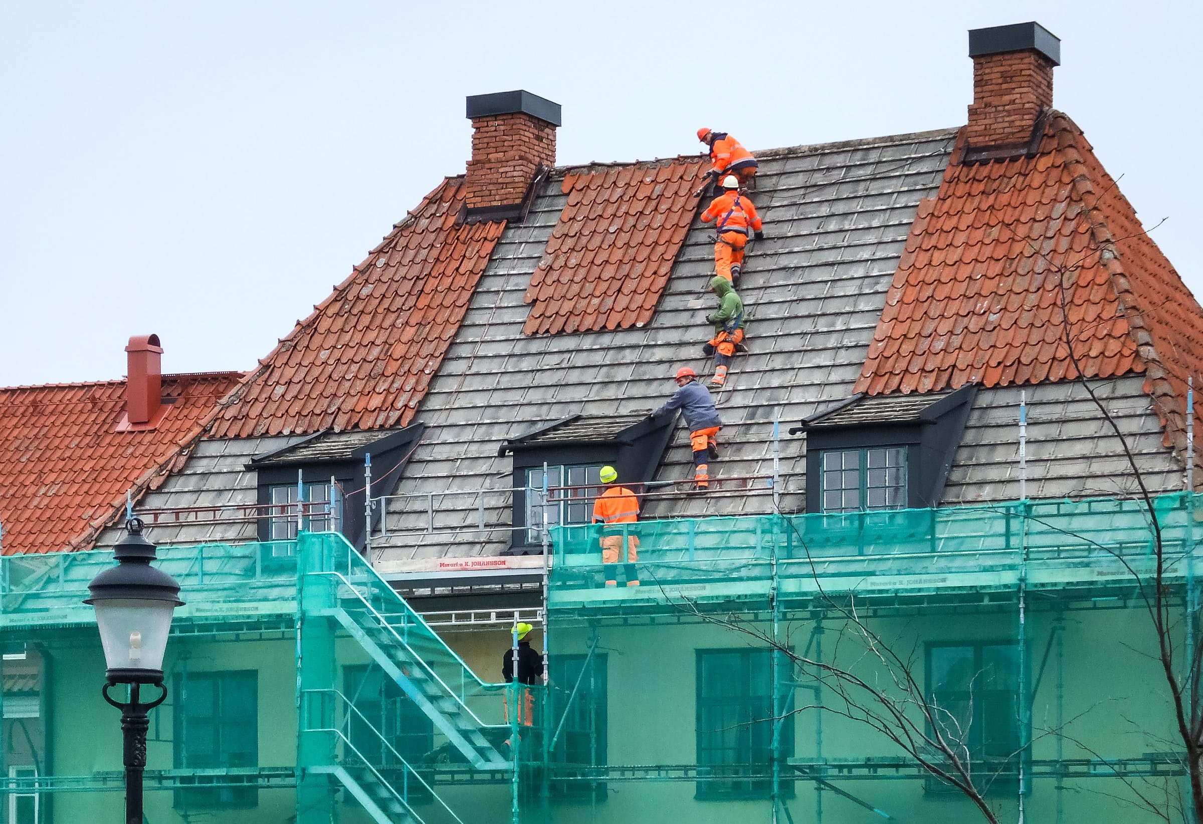 Roofers in orange high-visibility clothing replace tiles on a steep house roof at Södertorg in Visby.