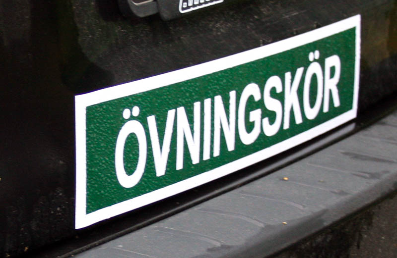 A green and white Swedish learner-driver sign attached to a car.