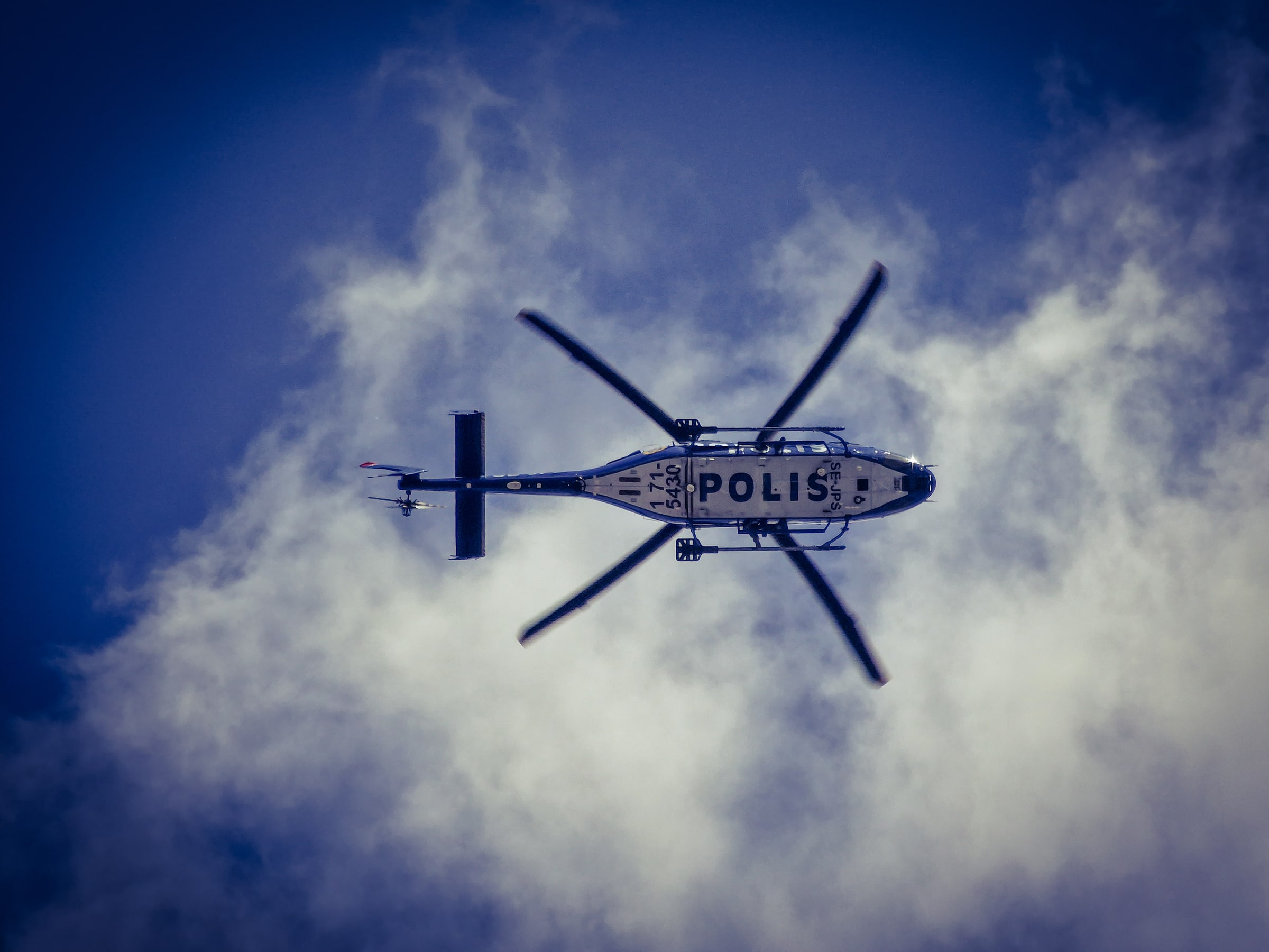 A Swedish police helicopter seen from below against blue sky and clouds