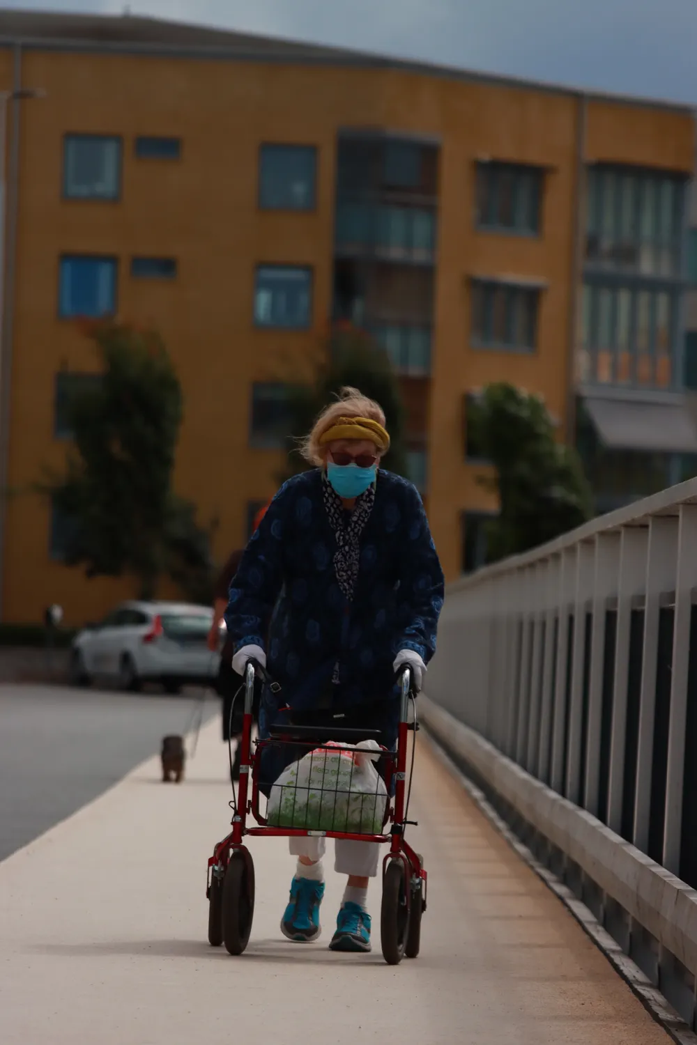 An older woman wearing a face mask walks with a rollator on a sidewalk in Jönköping.