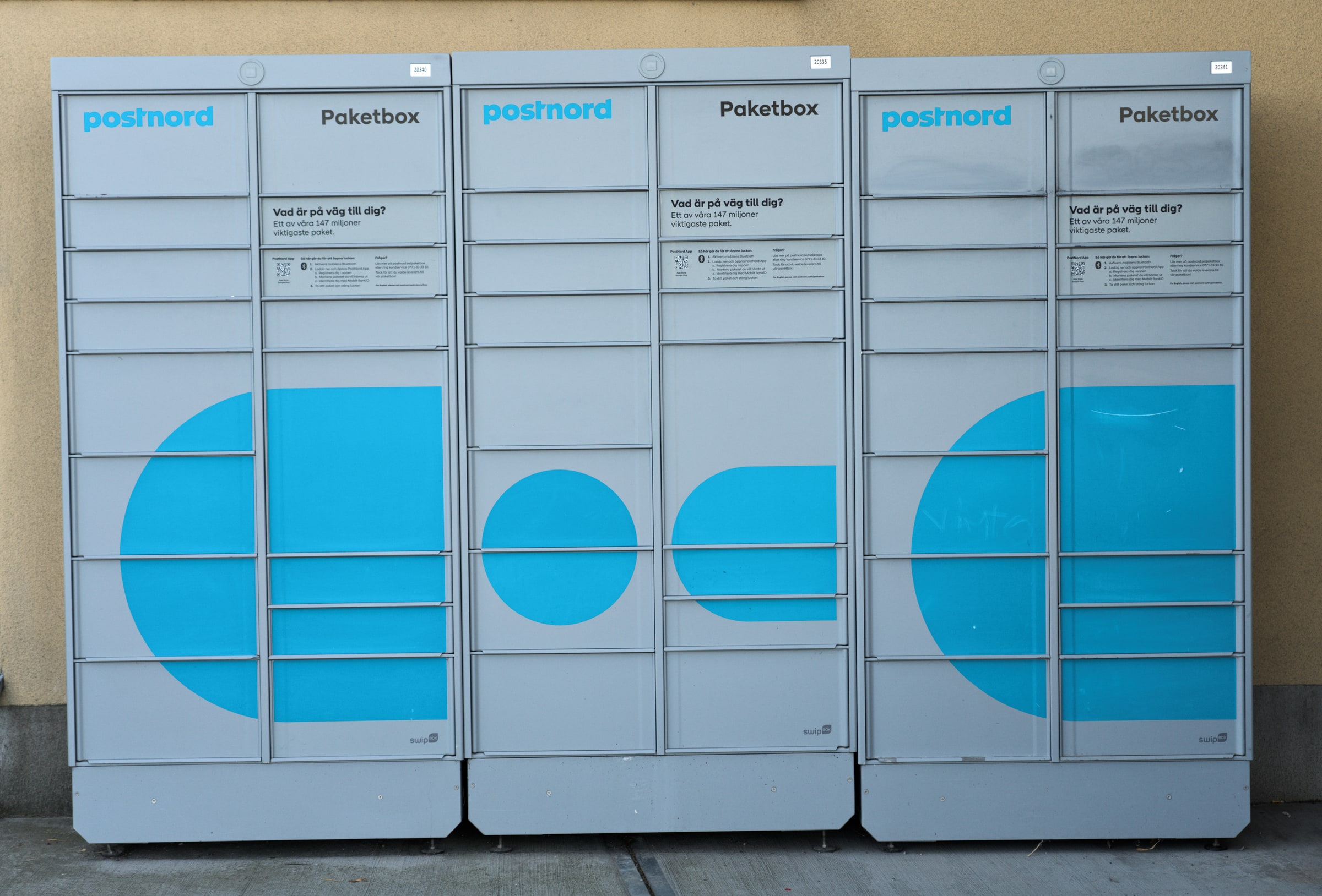 Grey PostNord parcel lockers stand against a wall in Stockholm.