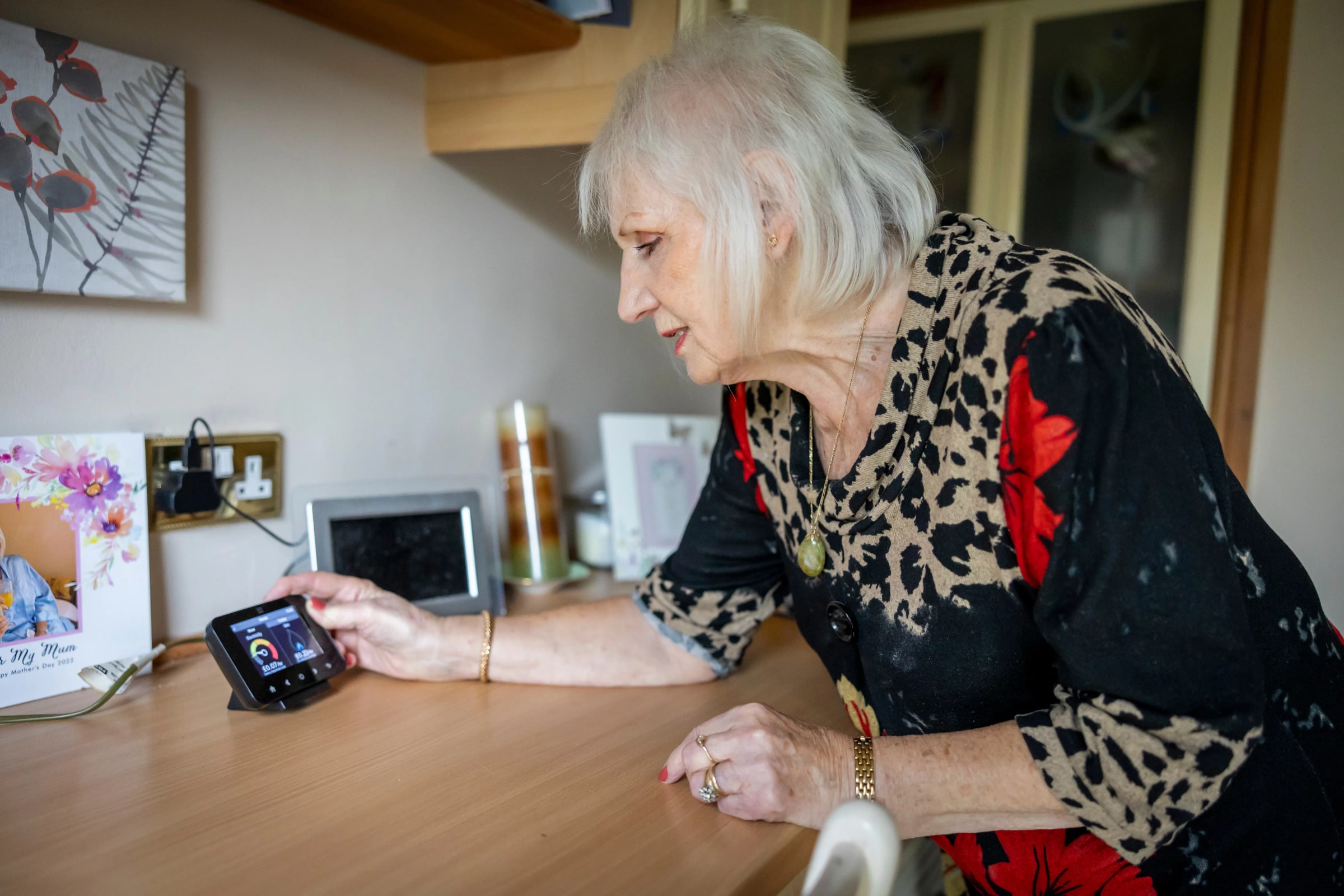 A woman leans over a desk to check a home energy monitor.