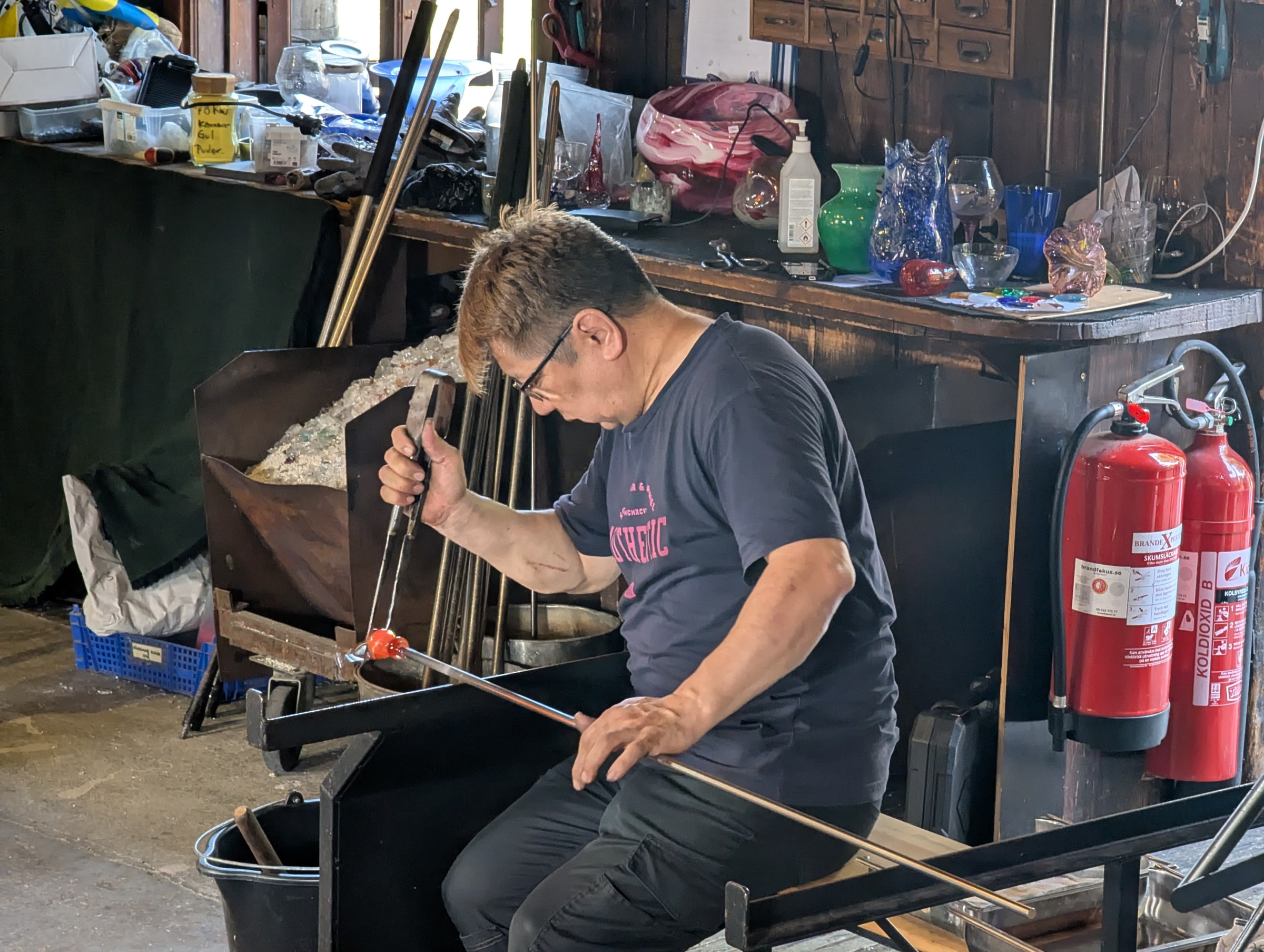 A glassworker shapes glowing glass with a hand tool at Skansen in Stockholm.