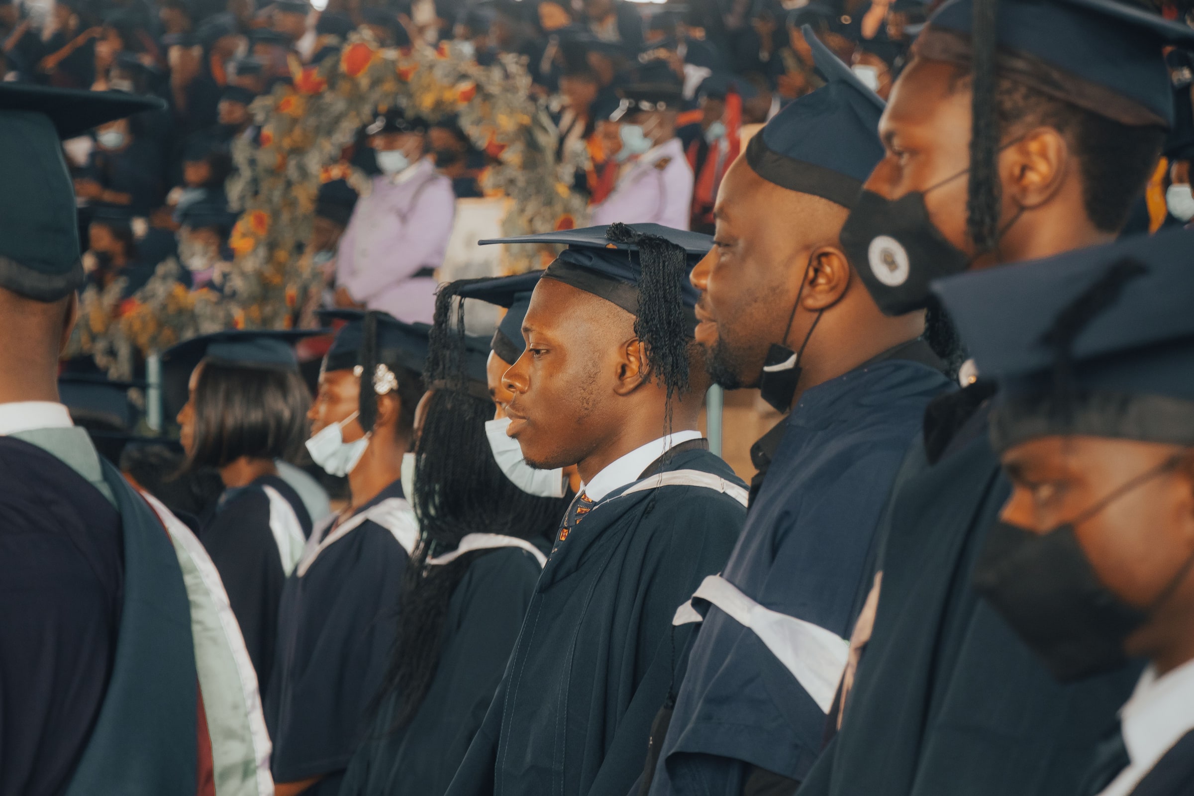 Graduates in black academic gowns and caps gather at a crowded ceremony in Nigeria.