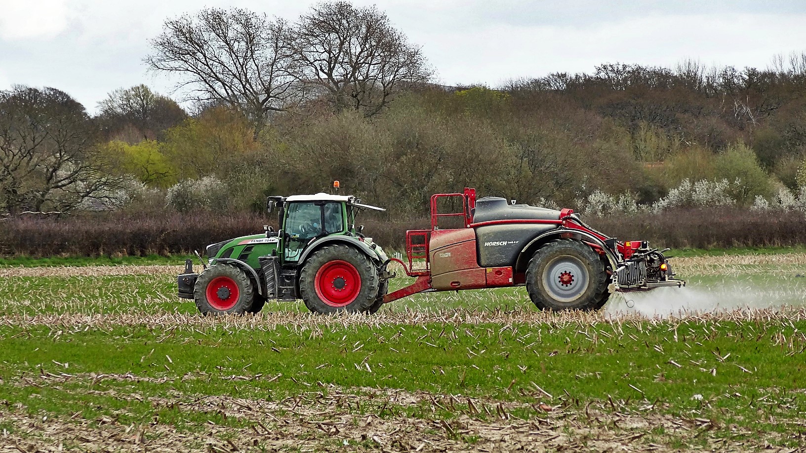 A tractor towing a crop sprayer applies liquid across a field in West Sussex, England
