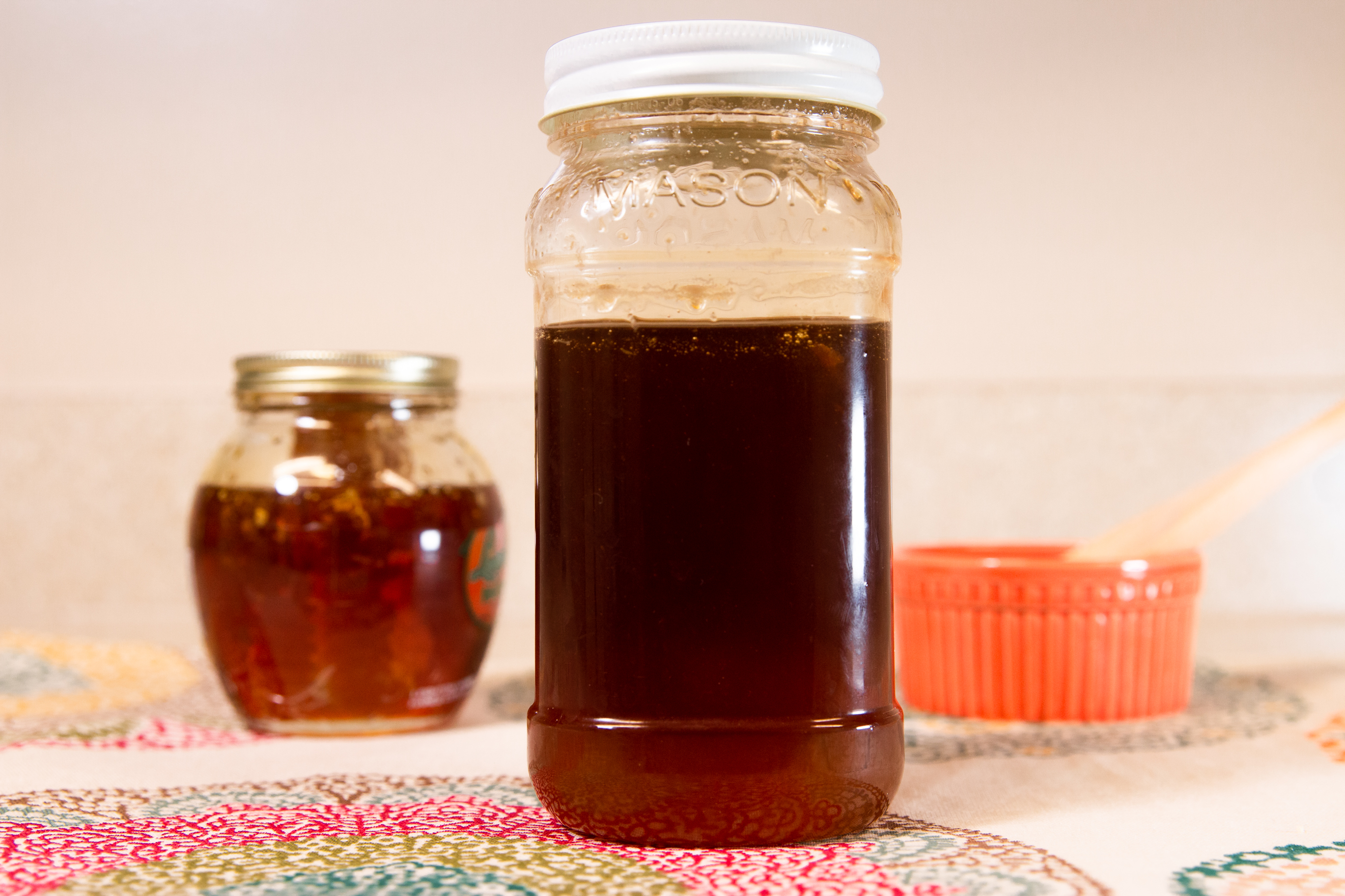 Two glass jars containing dark honey stand on a table.