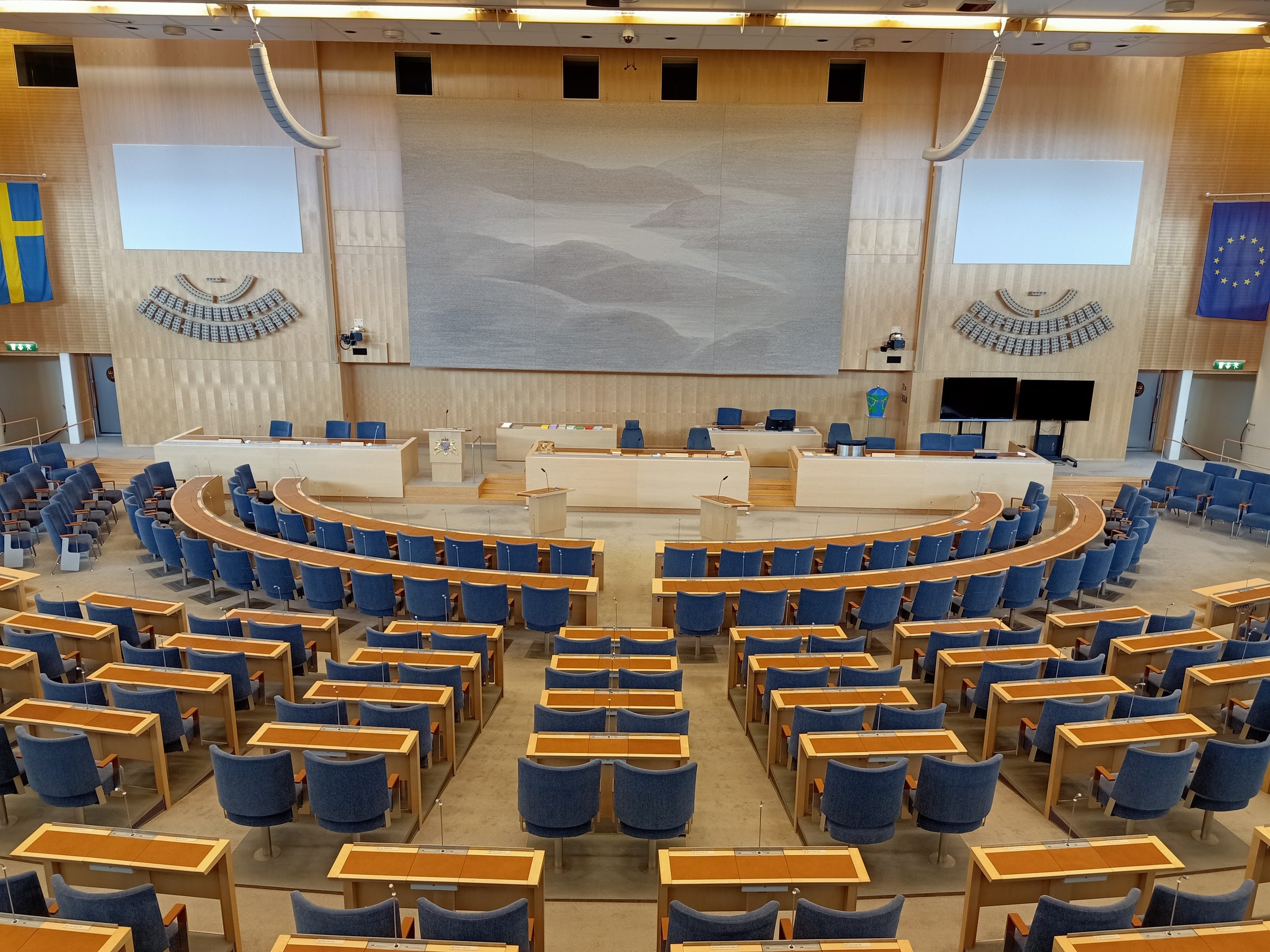 The empty Riksdag chamber in Stockholm, with blue seats and the speaking platform, photographed in August 2019.