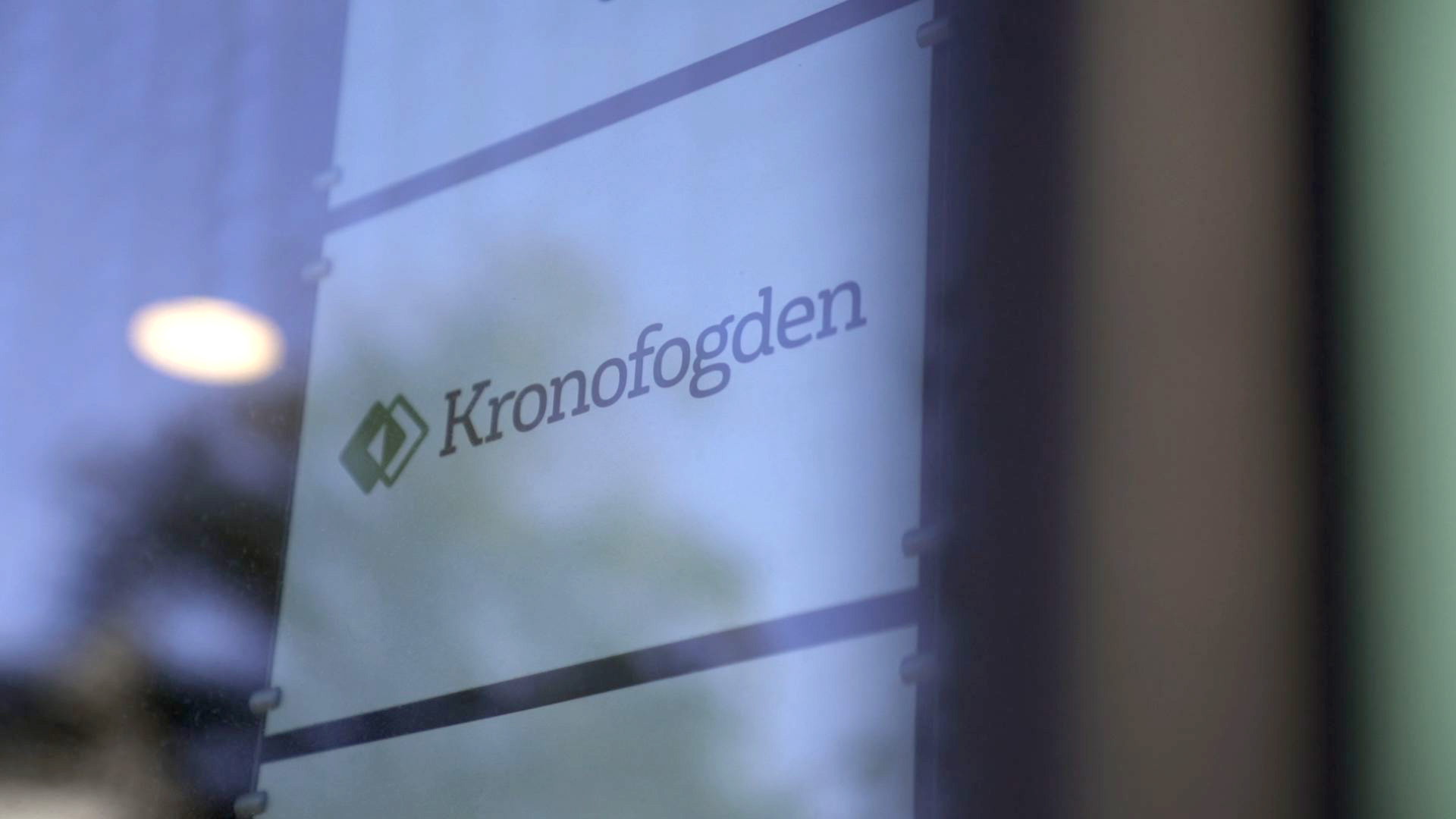 The Kronofogden name and symbol photographed on a translucent glass sign beside a window.