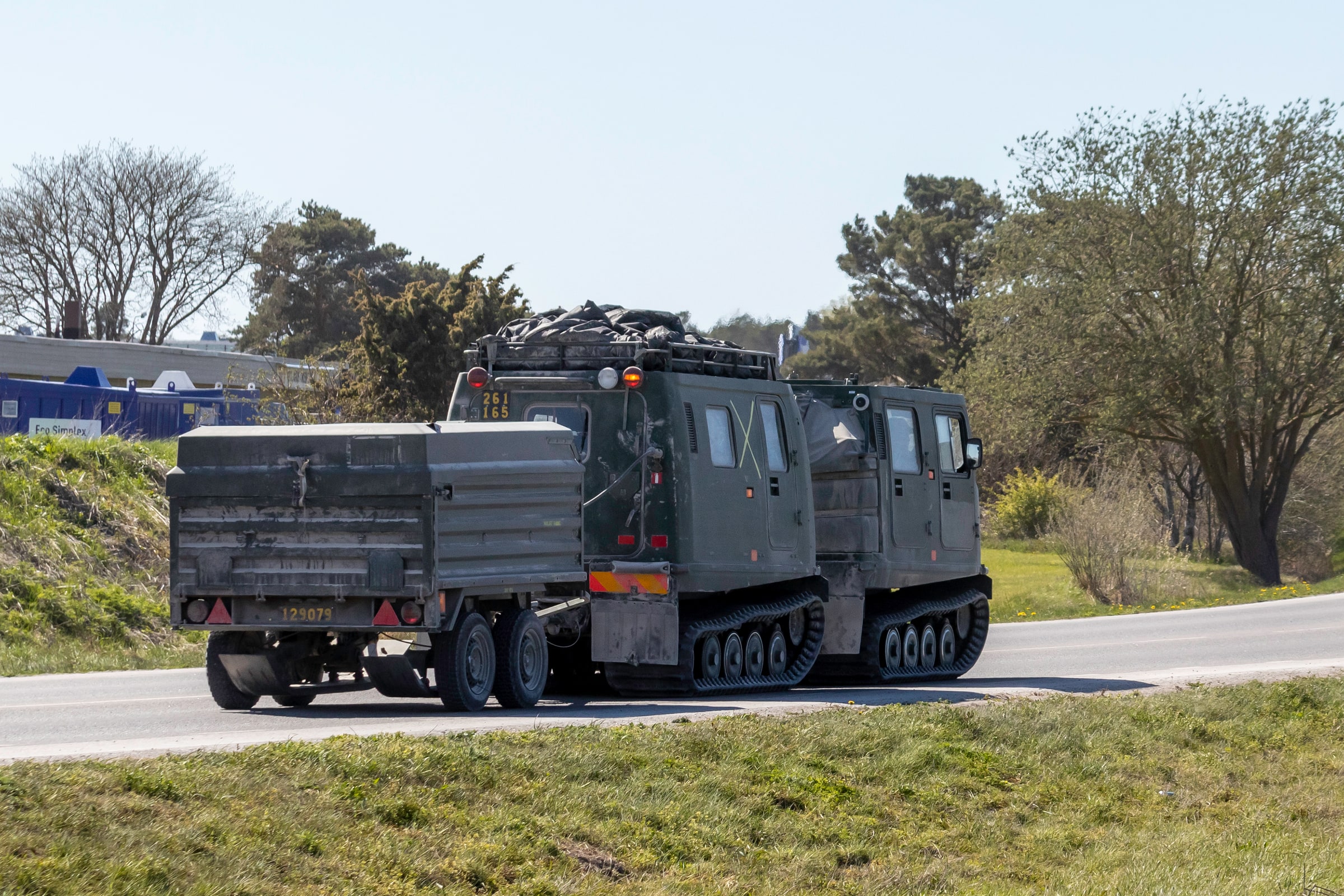 A Swedish tracked military vehicle pulls a loaded trailer on a road in Visby.