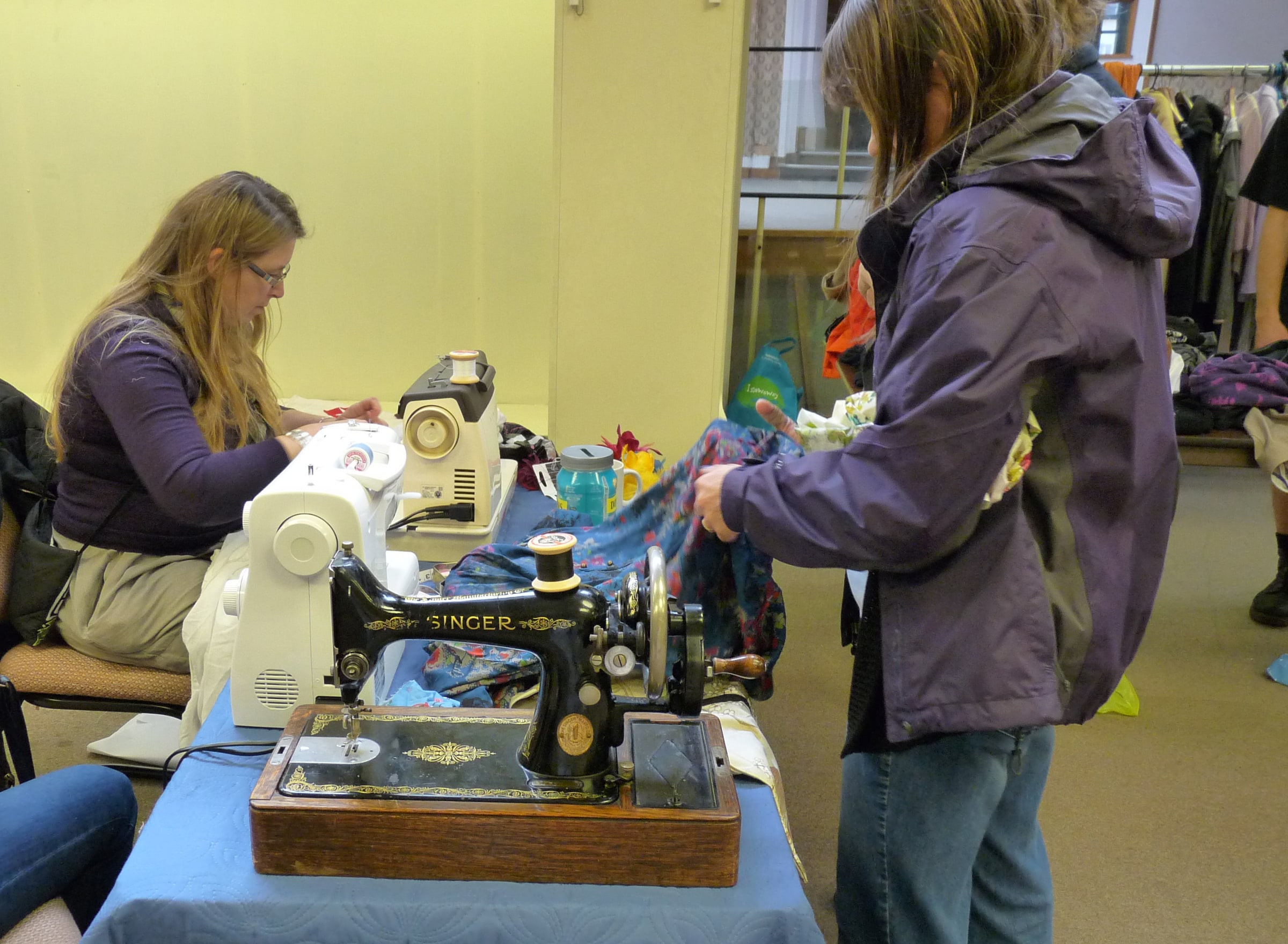 People use sewing machines to repair clothes and textiles at a community Repair Cafe.