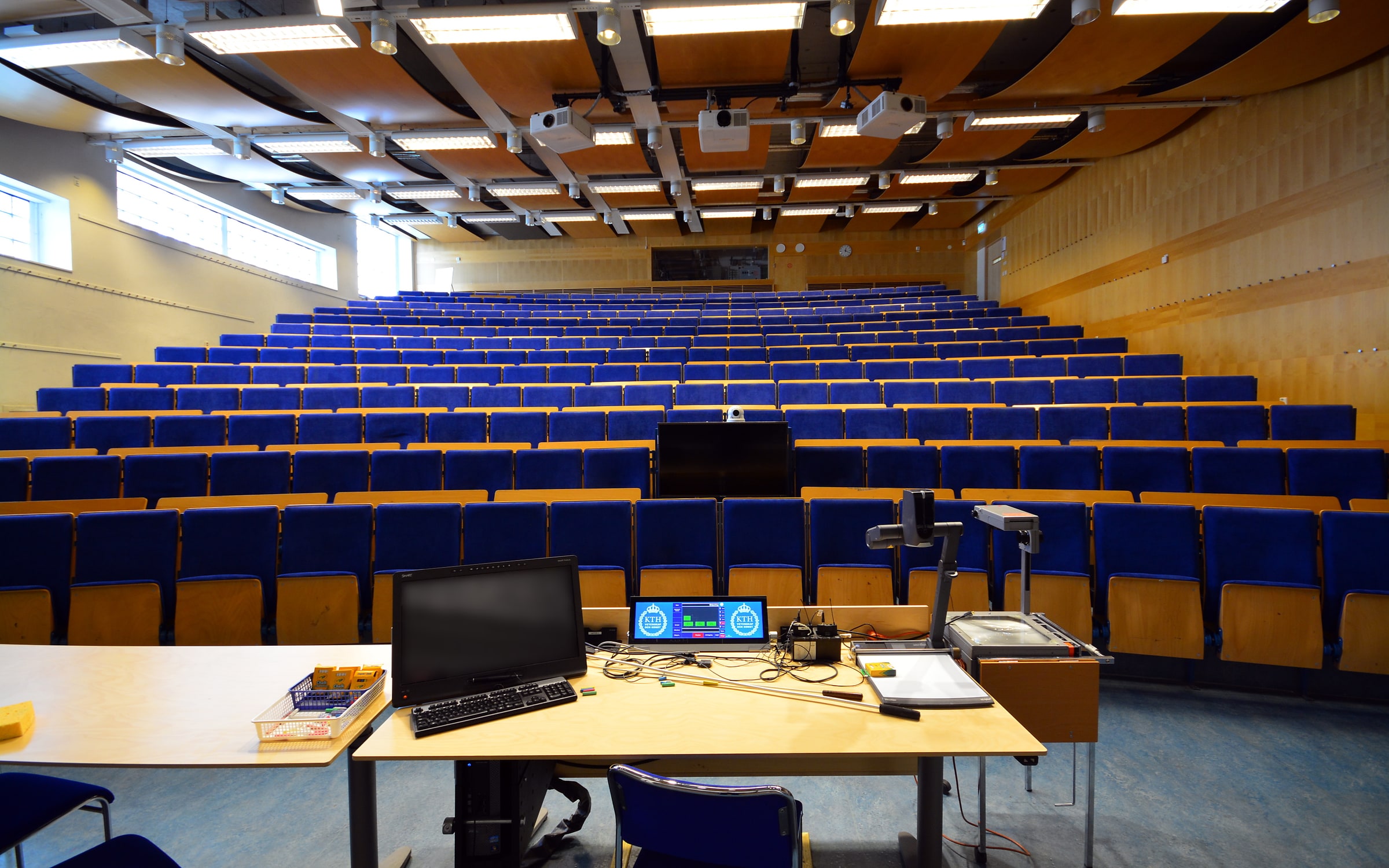 An empty KTH lecture hall in Stockholm with rows of blue seats facing teaching equipment.