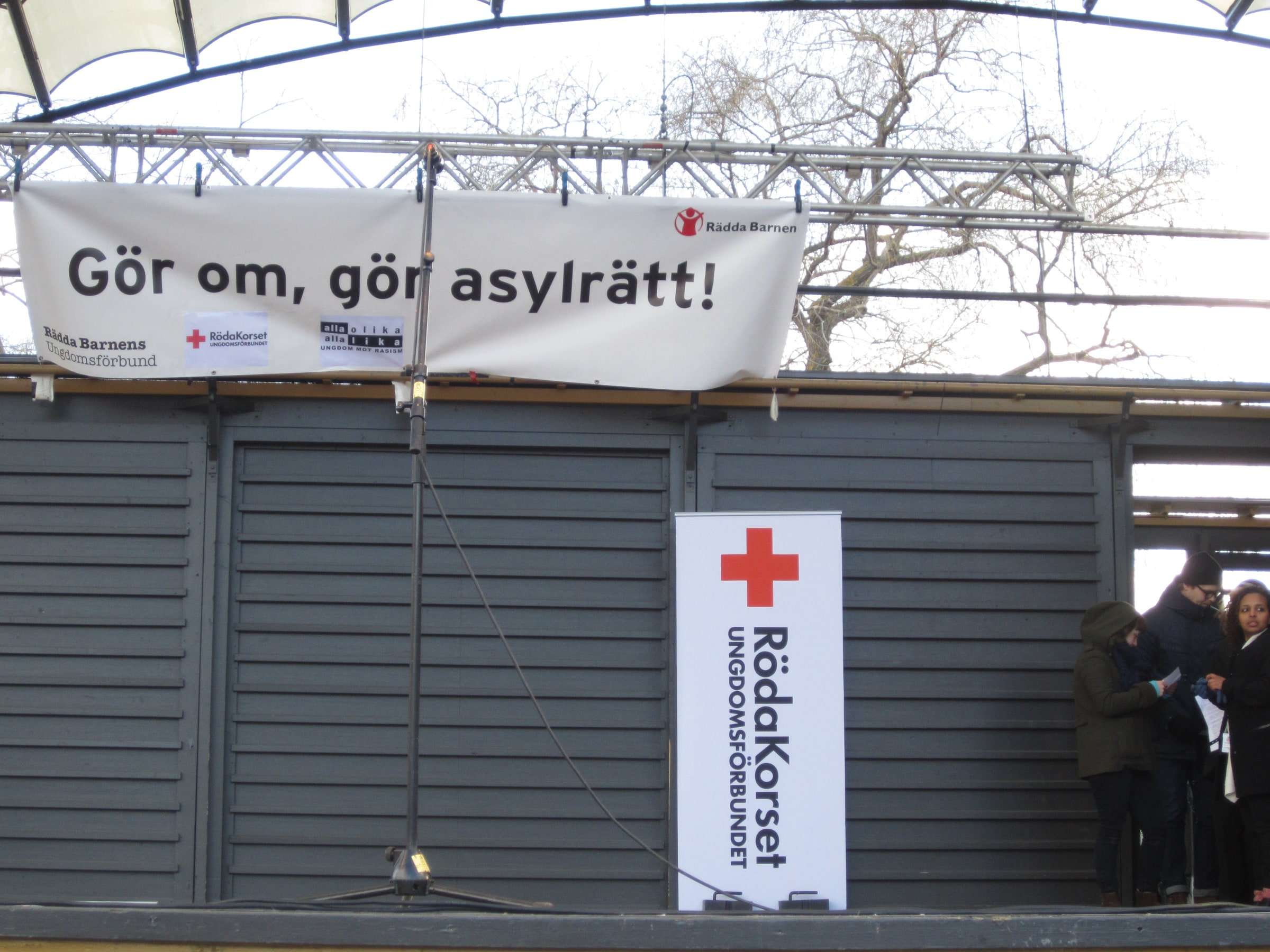 A Swedish asylum-rights banner above a Red Cross Youth lectern at a 2013 Stockholm demonstration.