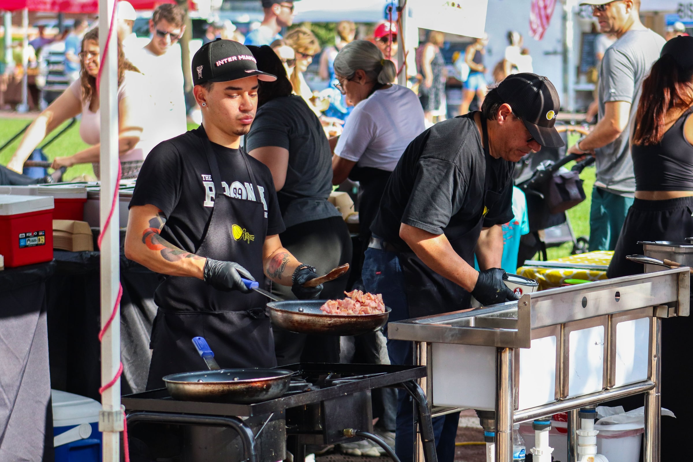 A cook prepares hot food at a busy outdoor festival.