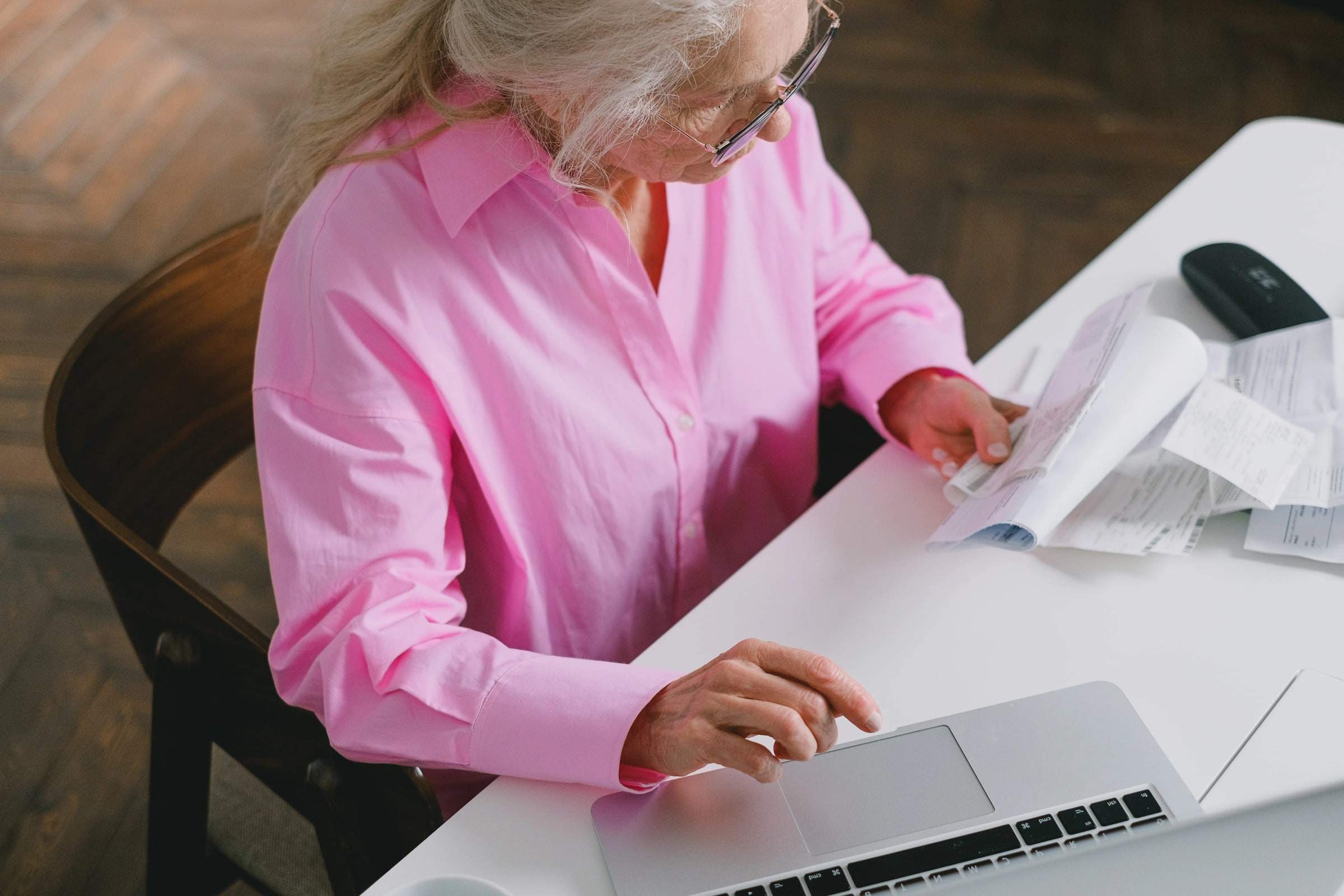 A woman reviews documents while using a laptop at a table.
