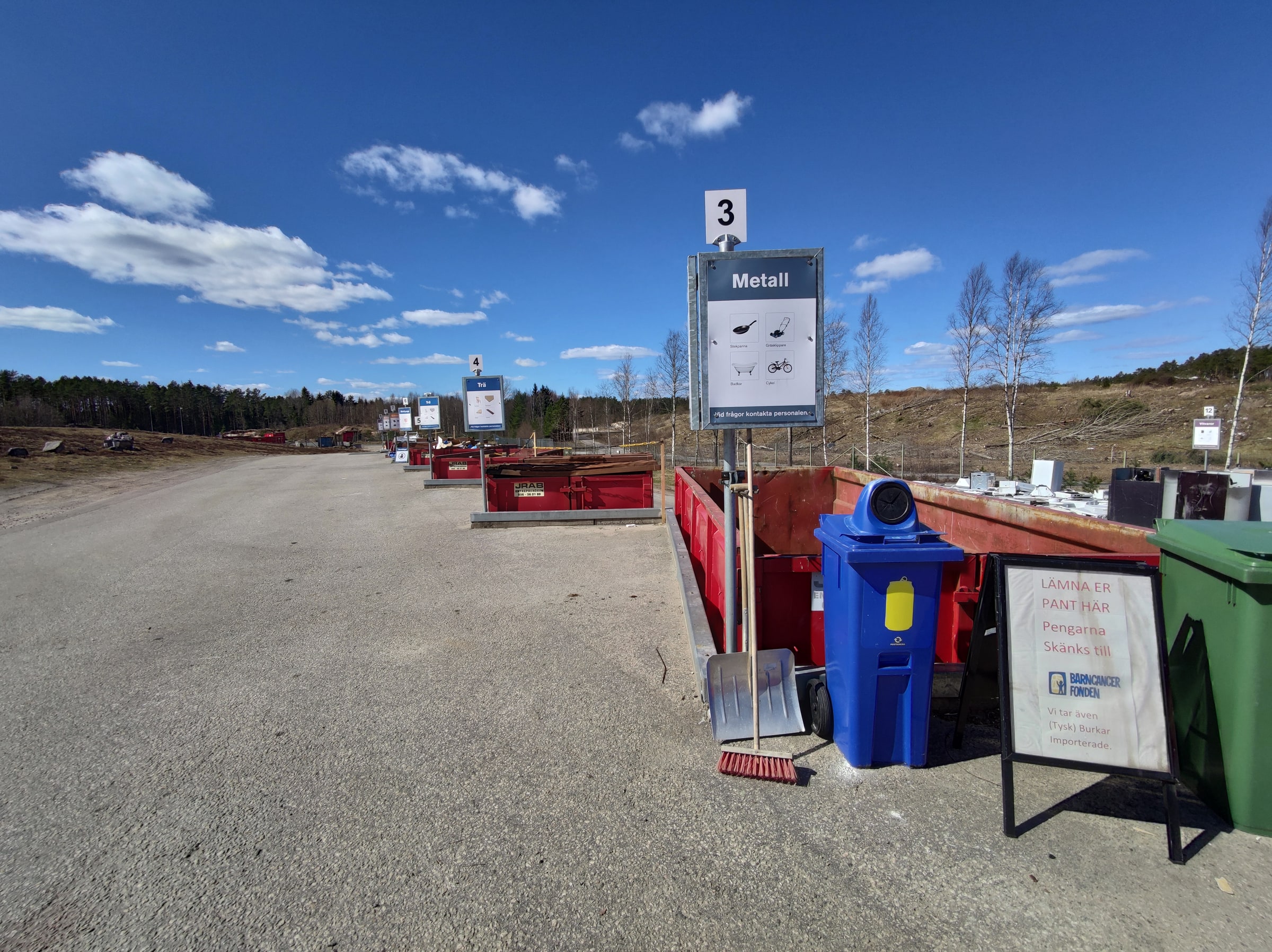 Metal collection containers and sorting signs line a Swedish recycling centre.