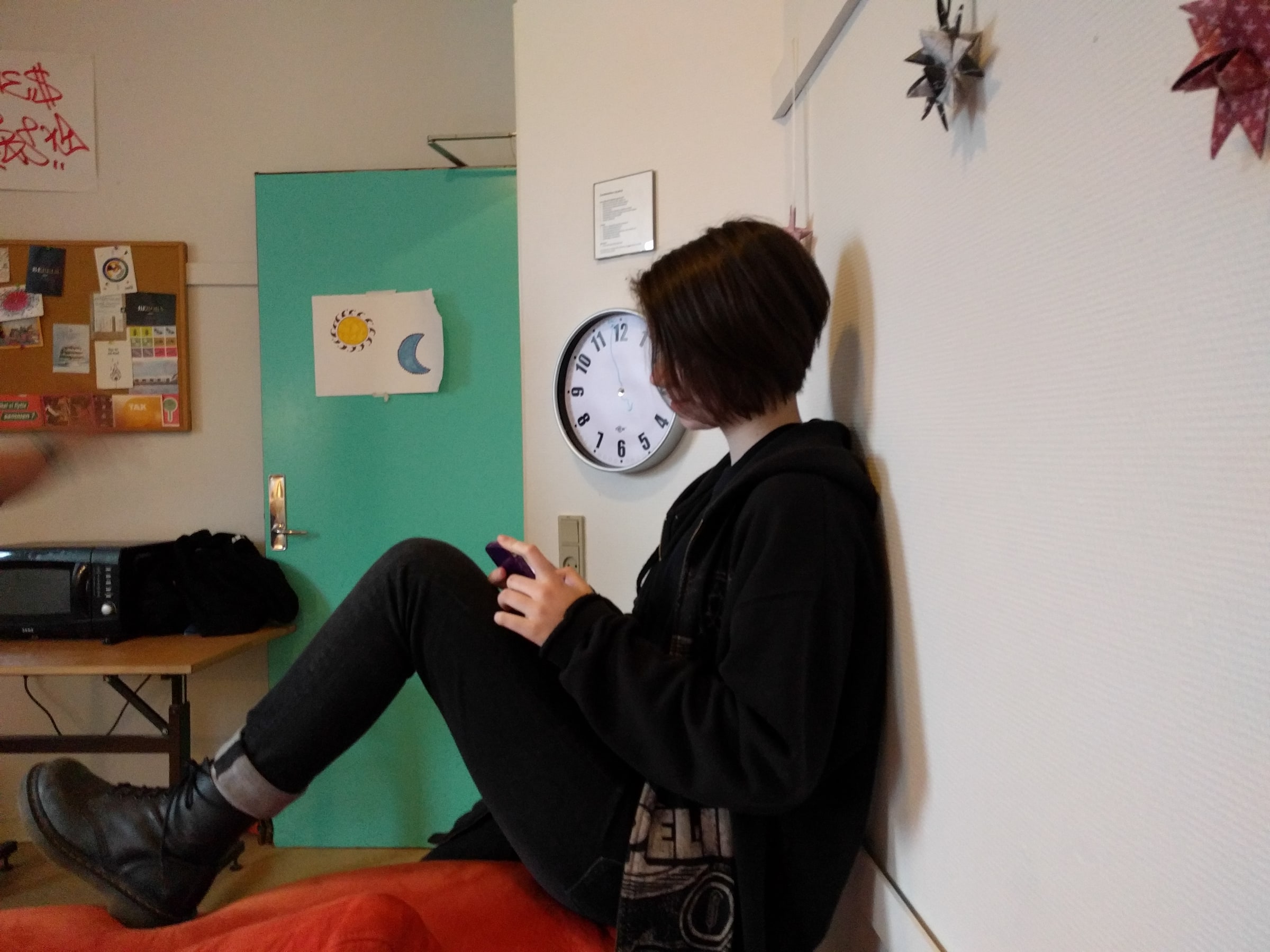 A teenager sits indoors while using a mobile phone.