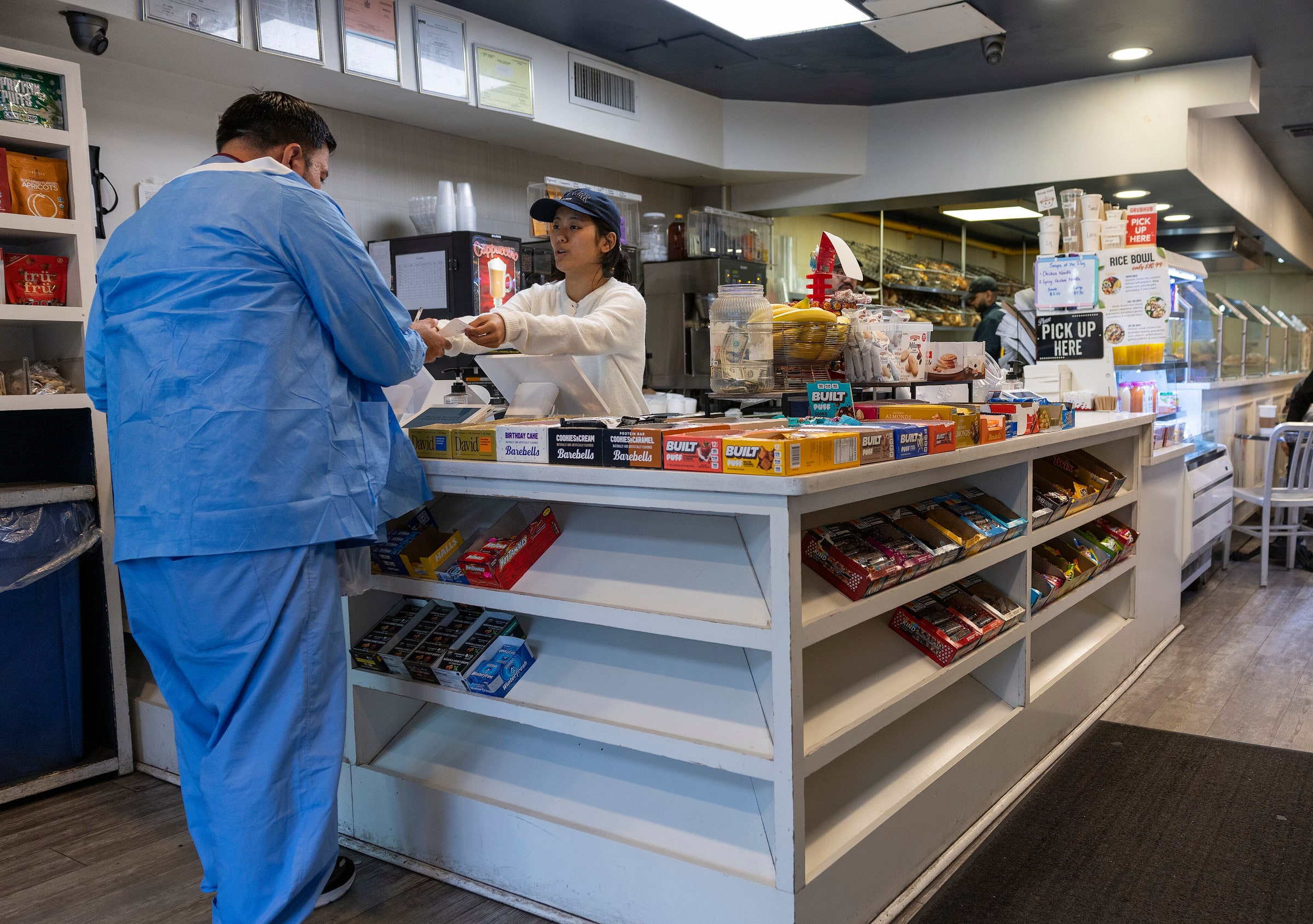A young cashier hands a receipt to a customer across a café counter.