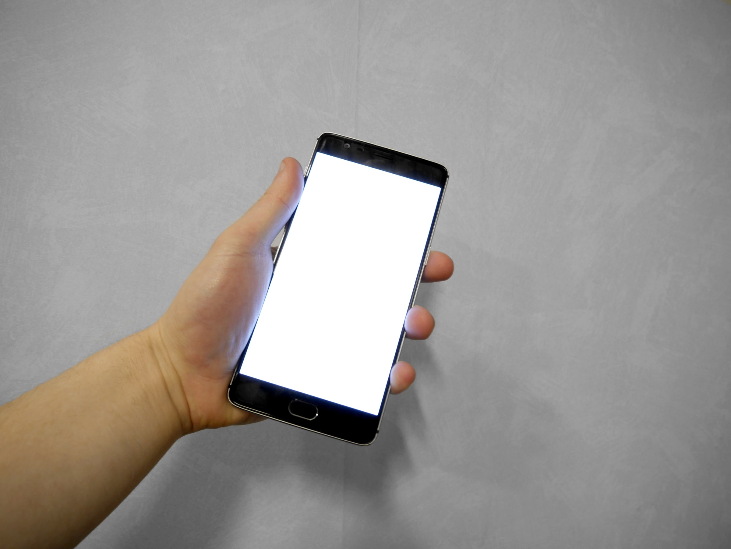 A hand holds a smartphone with a blank white screen.