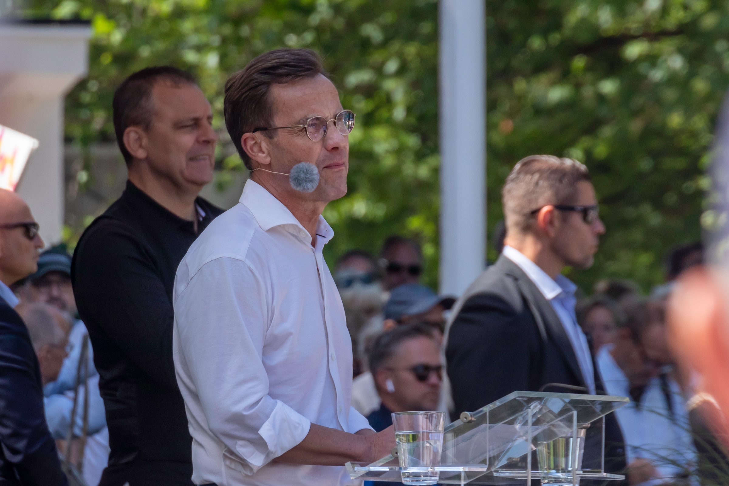 Ulf Kristersson stands at a transparent lectern wearing a headset microphone, with an audience behind him.