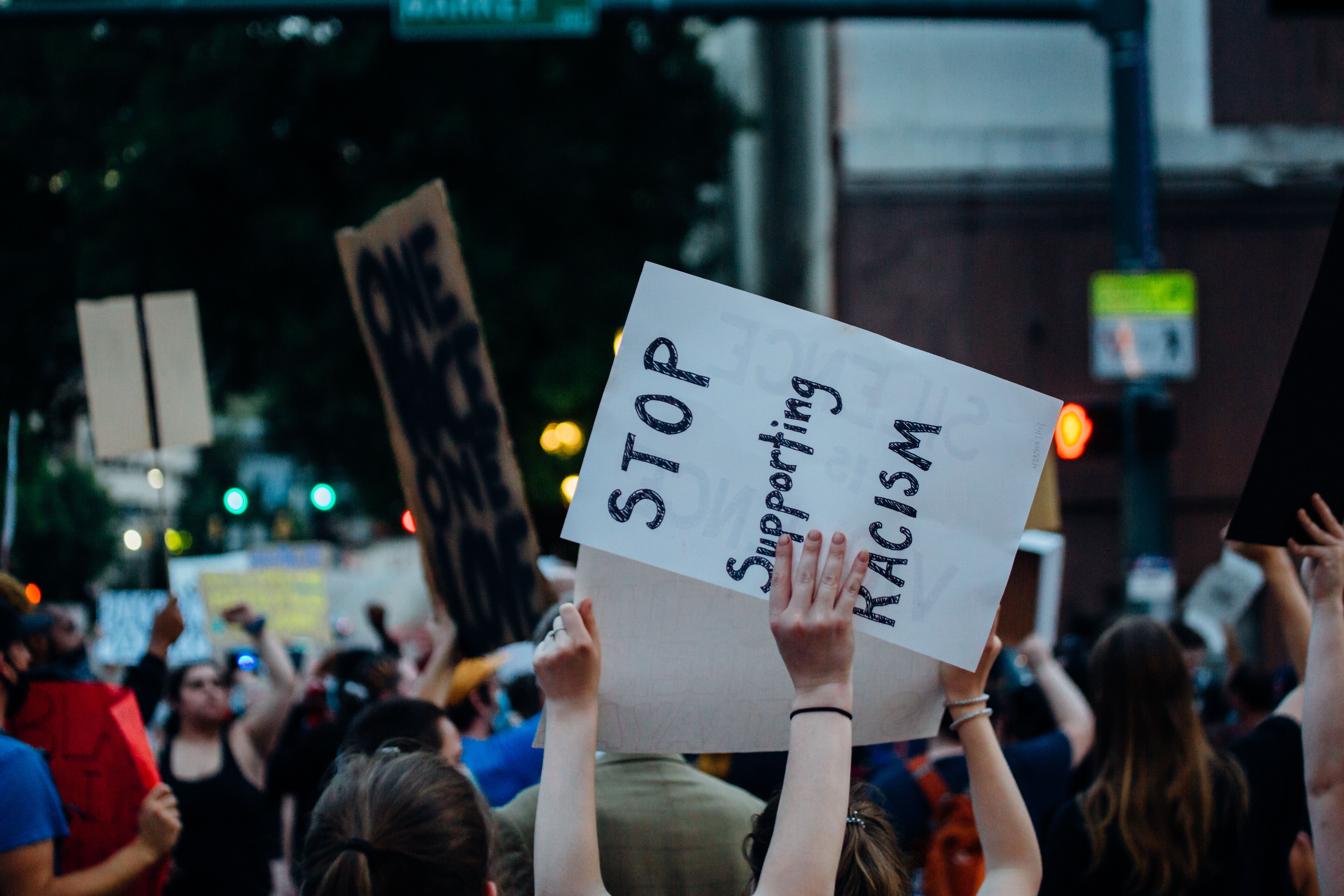 A crowd at an anti-racism demonstration holds signs opposing discrimination.