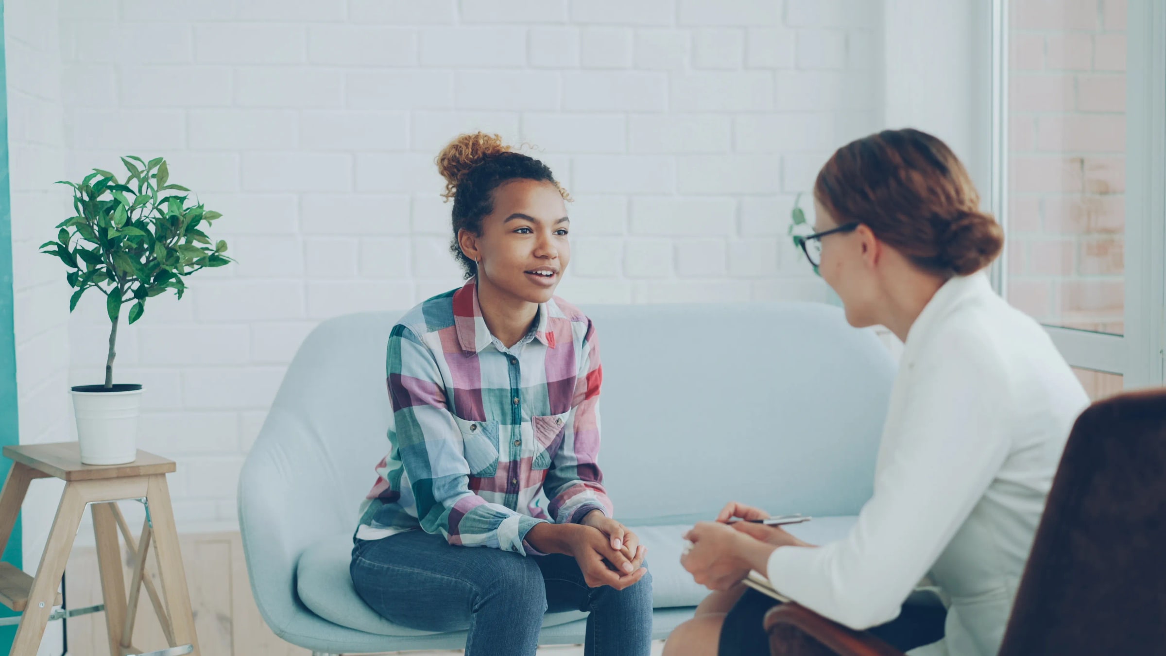A teenager talks with a therapist in a bright counselling room.