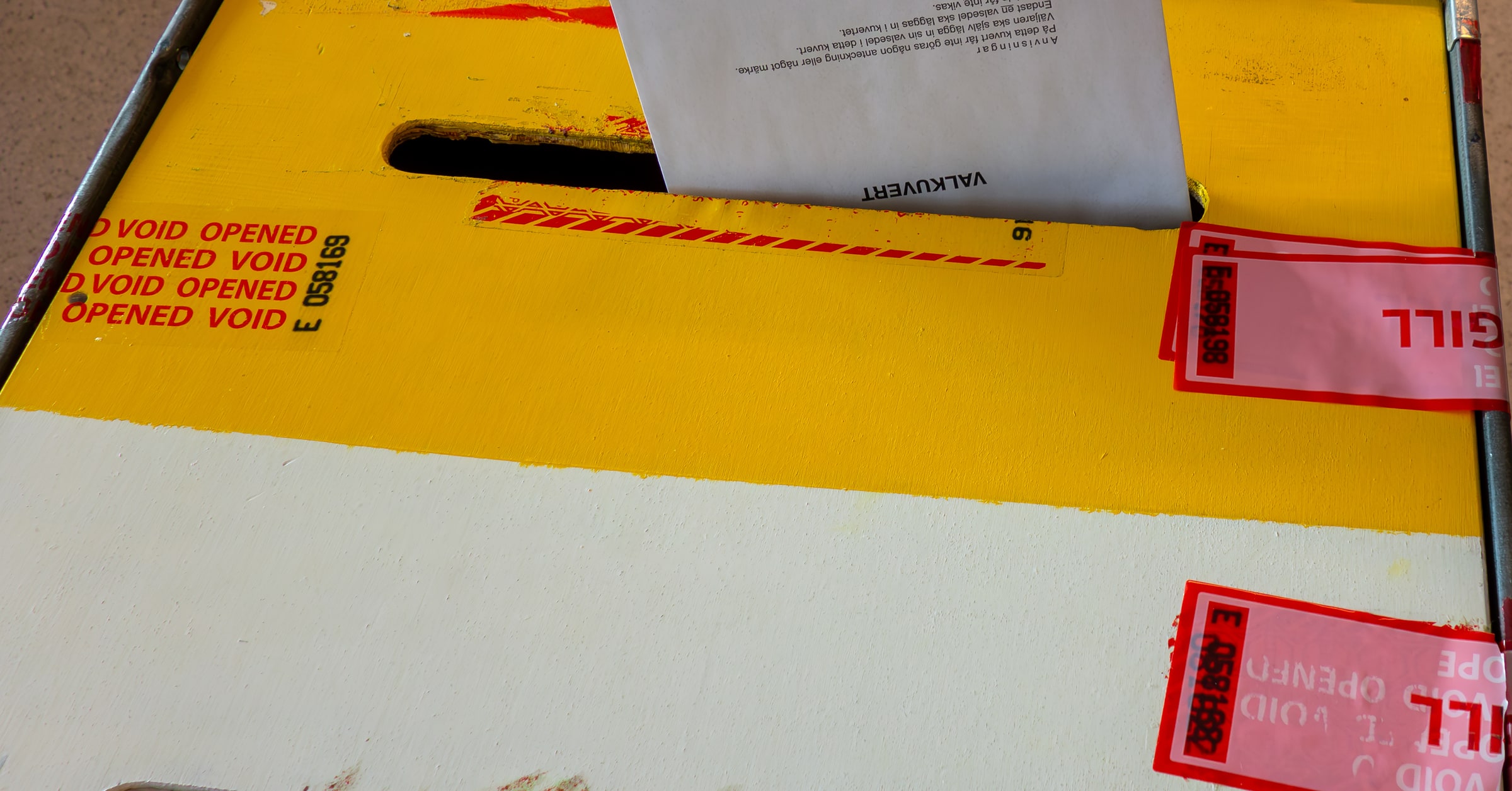 A ballot envelope at the slot of a sealed yellow and white ballot box.