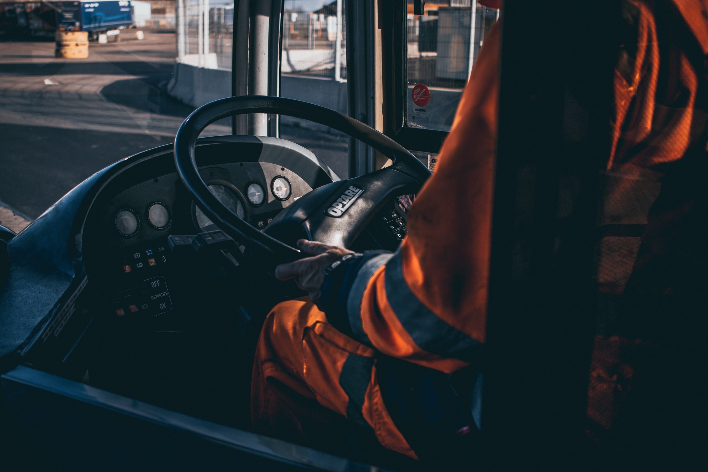 A bus driver in orange reflective clothing holds the steering wheel inside a bus.