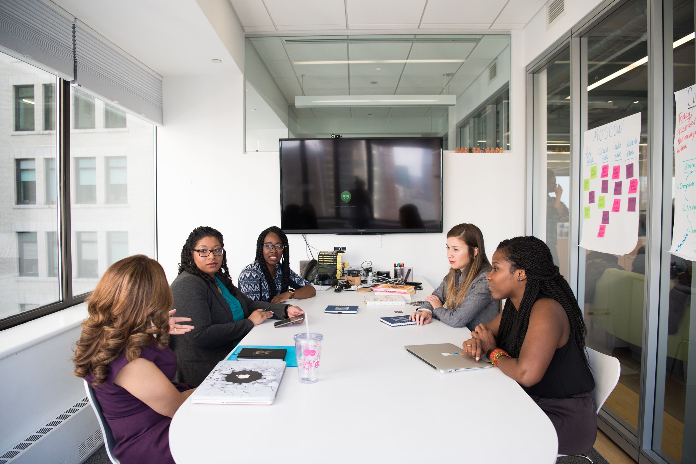 Five women meet around a conference-room table.