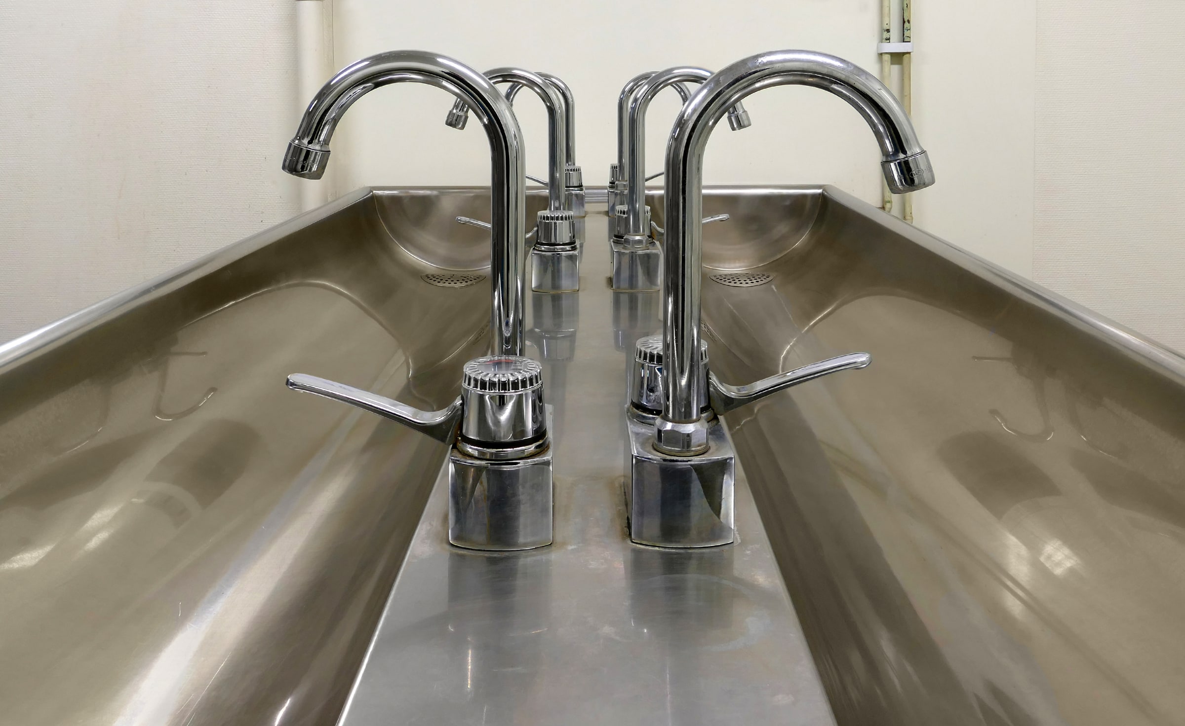 Chrome taps above stainless-steel washbasins in a workshop washroom in Gåseberg, Sweden.