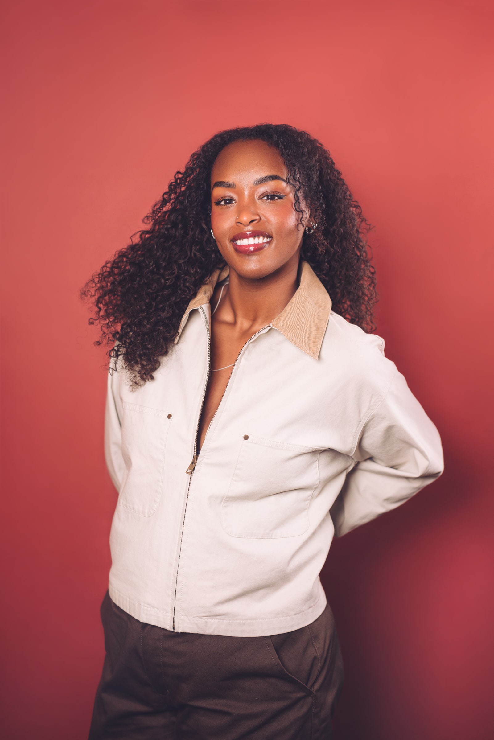 Assia Dahir smiles against a red background in a 2026 press portrait.
