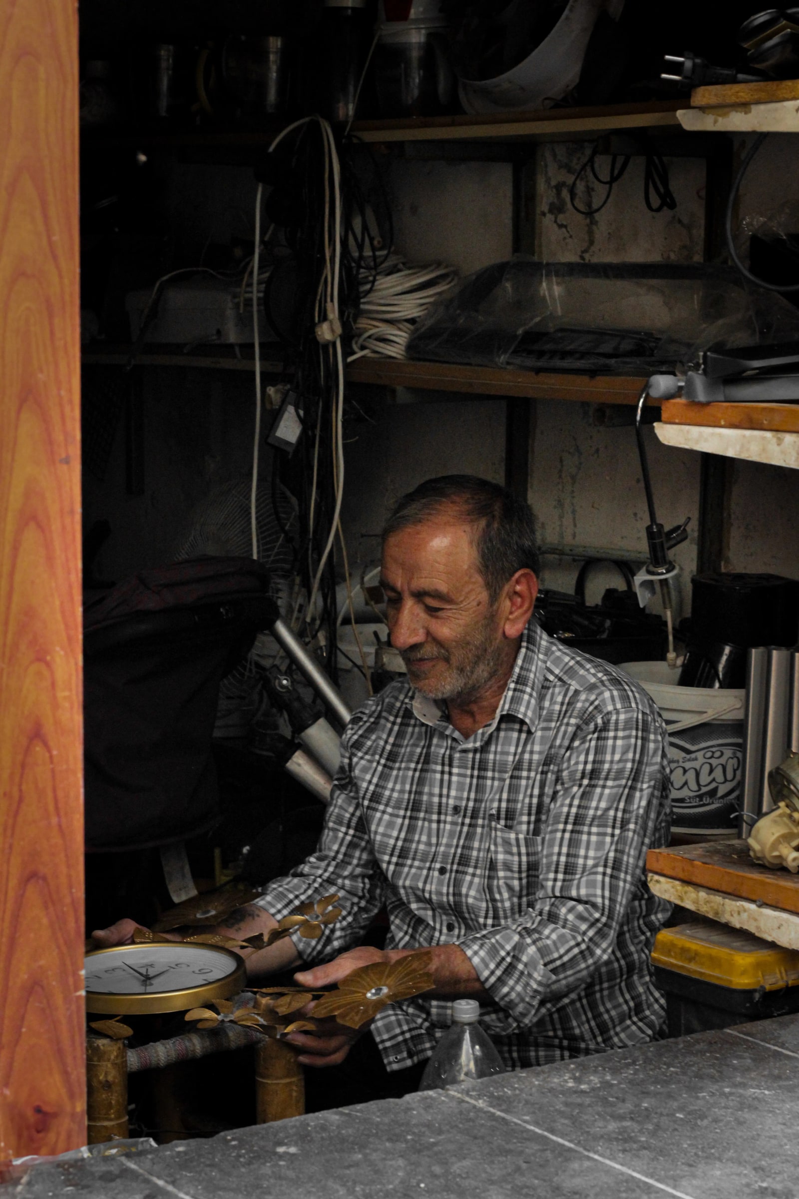 Hands handling clock parts in a workshop filled with tools.