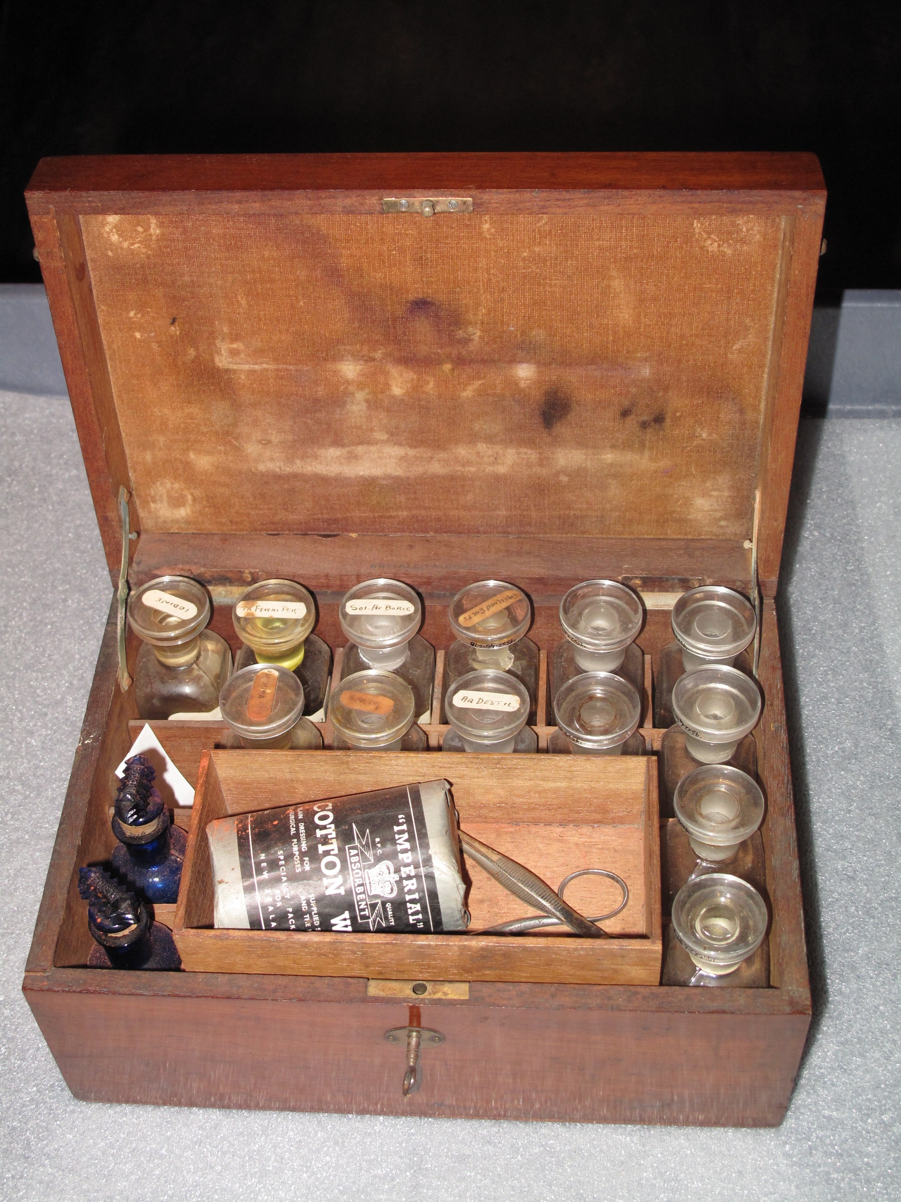 An open wooden historical medicine box with glass bottles and a key in its front lock.
