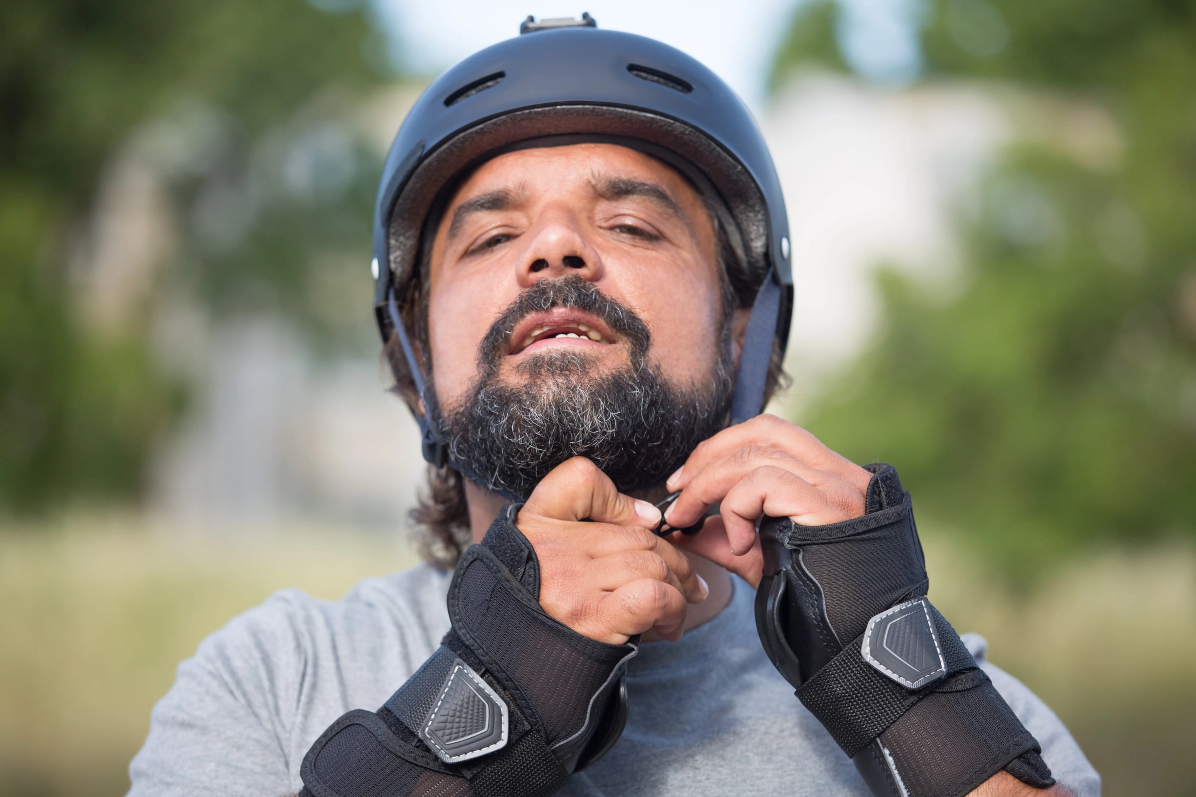 A man fastens the chin strap of a black cycling helmet outdoors.