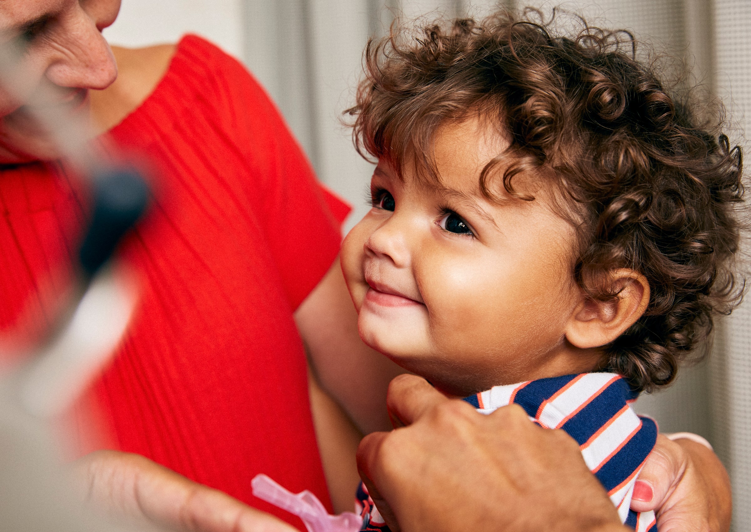 A smiling toddler is held by an adult while receiving a vaccination.