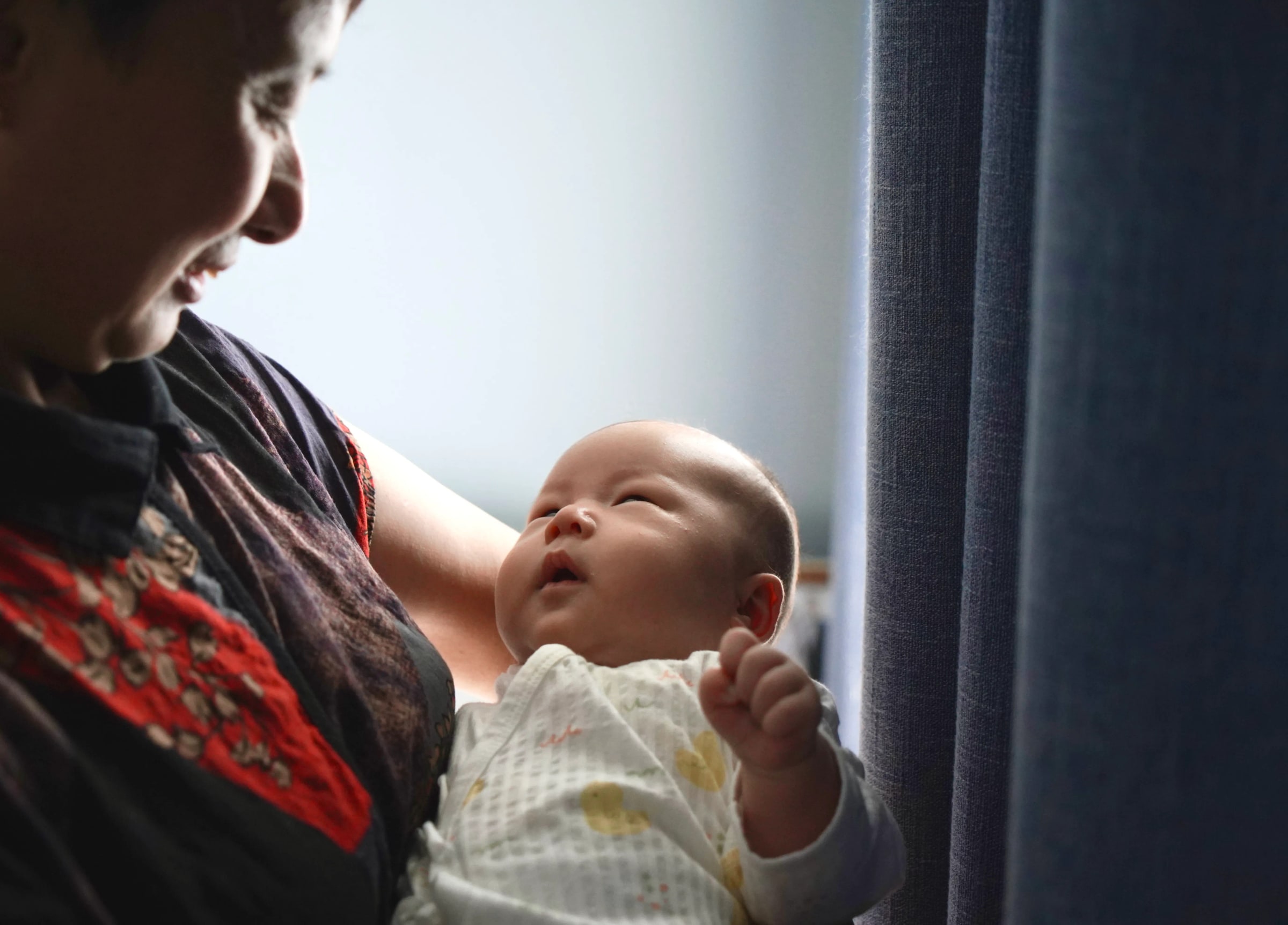 A grandmother cradles a newborn beside a window.