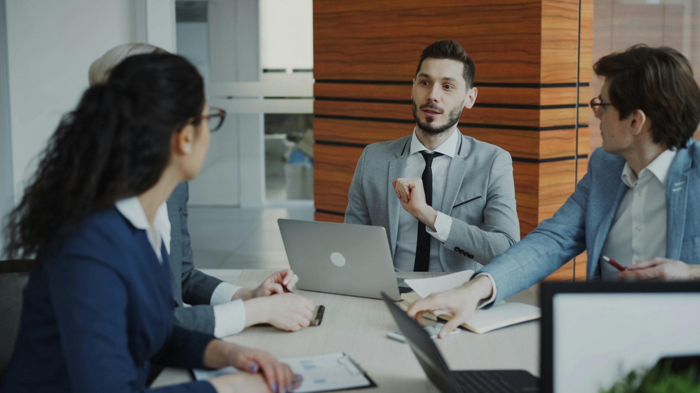 Four business professionals discuss documents around a laptop at a meeting table.