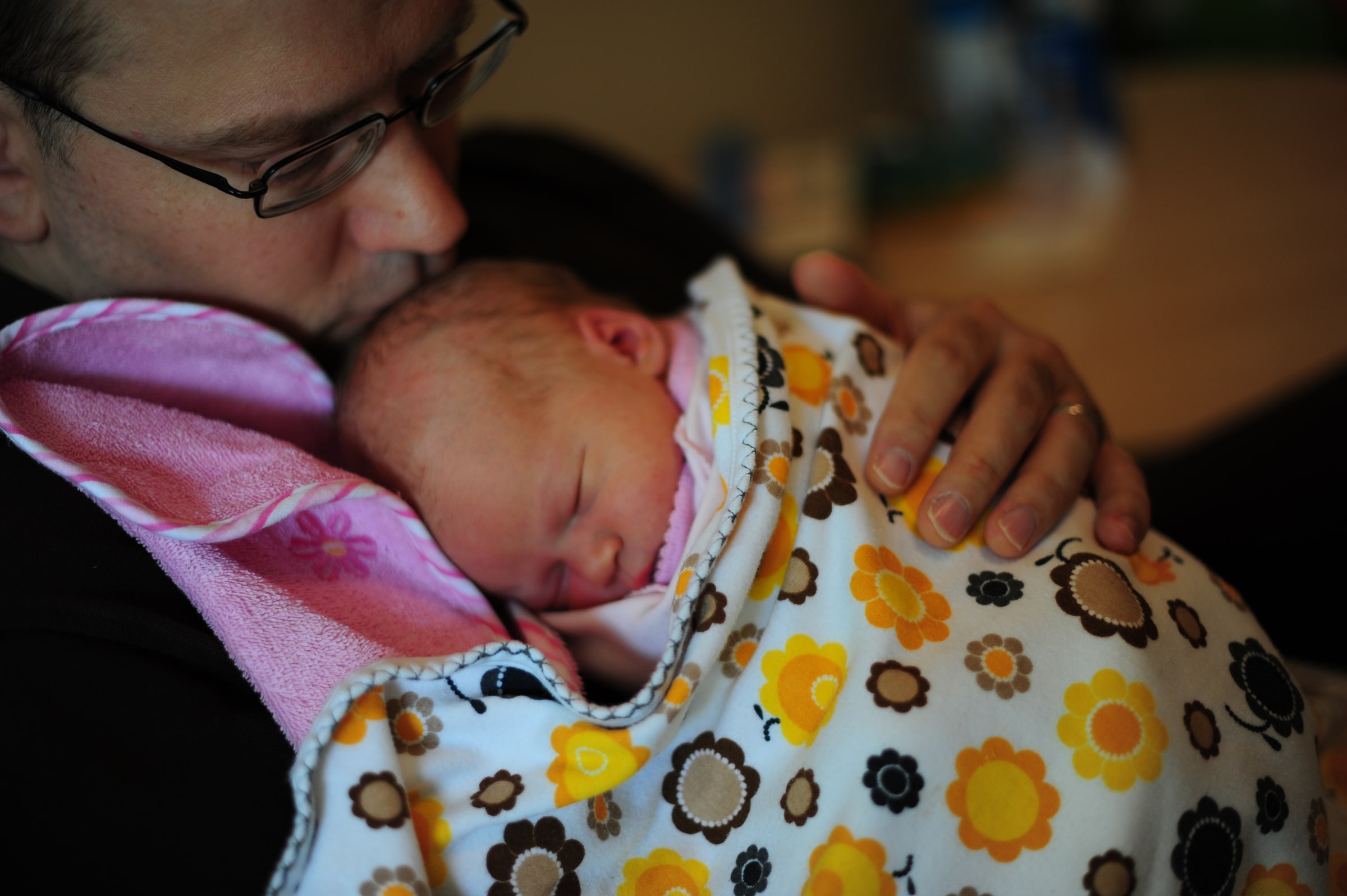 A father holds and cuddles a sleeping newborn wrapped in patterned blankets.